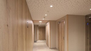 A hallway with wooden walls and doors, a tiled floor, and a ceiling with recessed lighting.