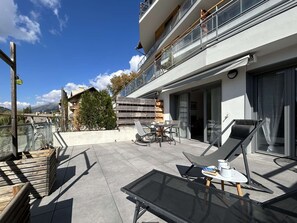 A modern outdoor patio with a glass table, lounge chairs, and a wooden deck. - Cosy 2-Room Apartment in Briançon, Terrace, 4 Guests, WiFi, Parking, 3-Star Rating (Briançon)
