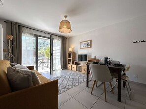 A modern living room with a sofa, a dining table with chairs, a TV, and a lamp.