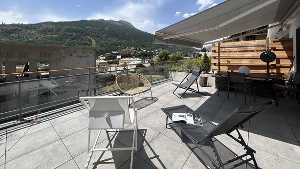 A rooftop terrace with lounge chairs, a table, and a dartboard.