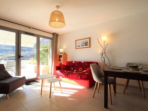 Uma sala de estar moderna com um sofá, cadeiras, uma mesa de jantar e uma grande porta de vidro deslizante que dá para uma área externa.