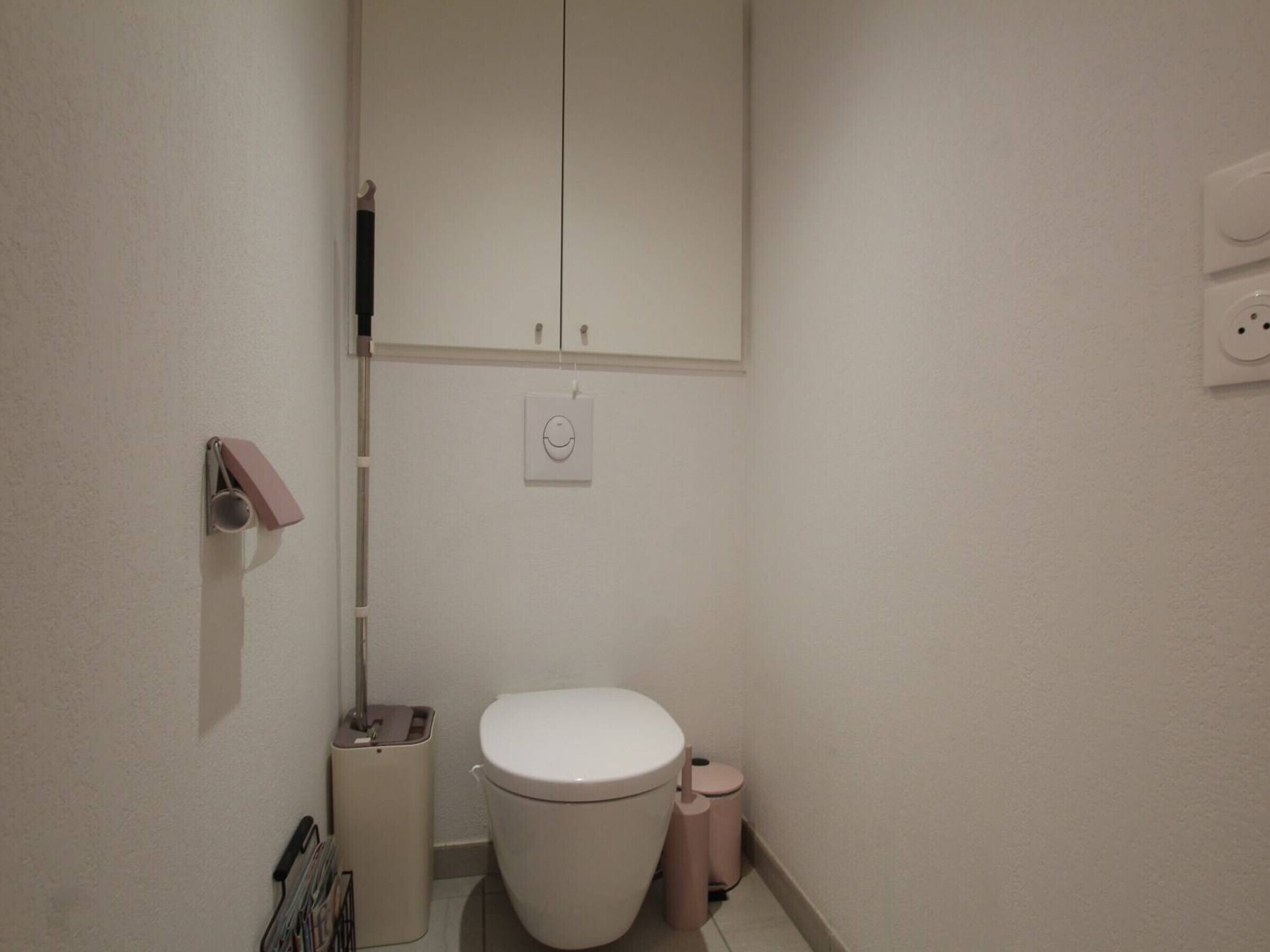 A small, clean bathroom with a toilet, a trash bin, and a towel rack.