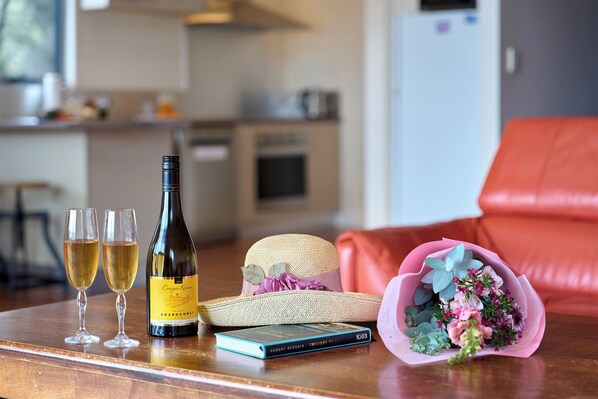 A table with two glasses of wine, a bottle of chardonnay, a book, and a bouquet of flowers.