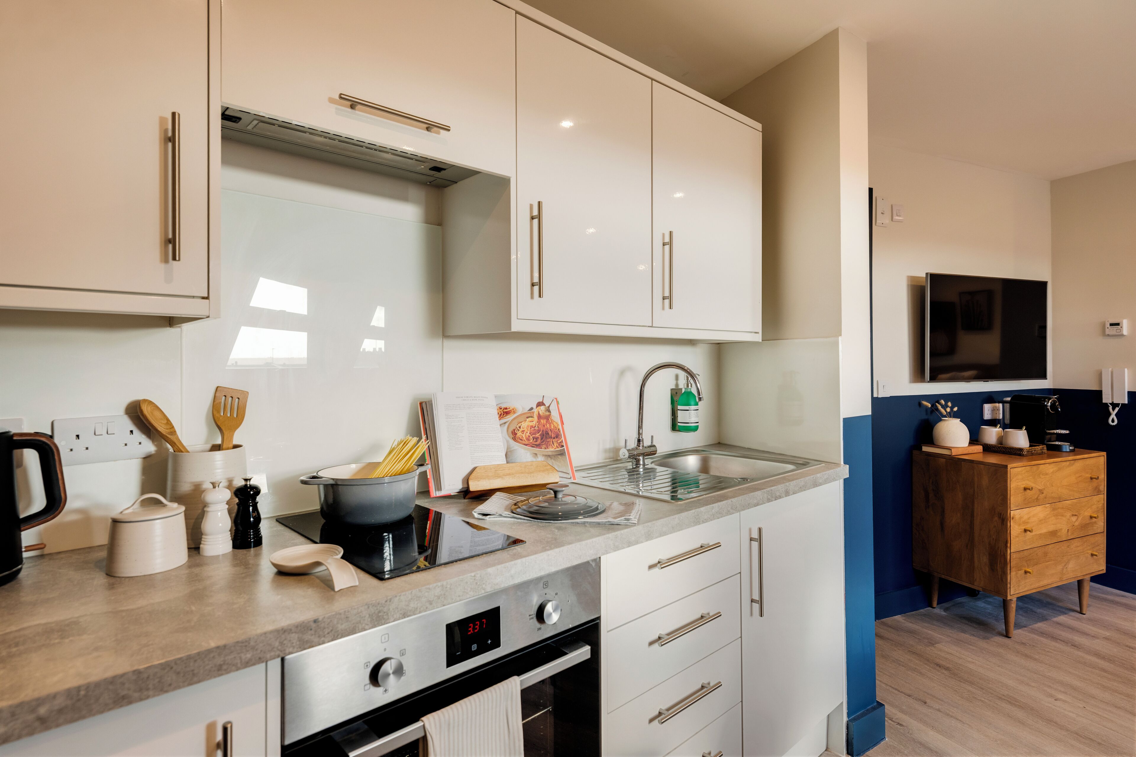A modern kitchen with white cabinets, stainless steel appliances, and a wooden sideboard.