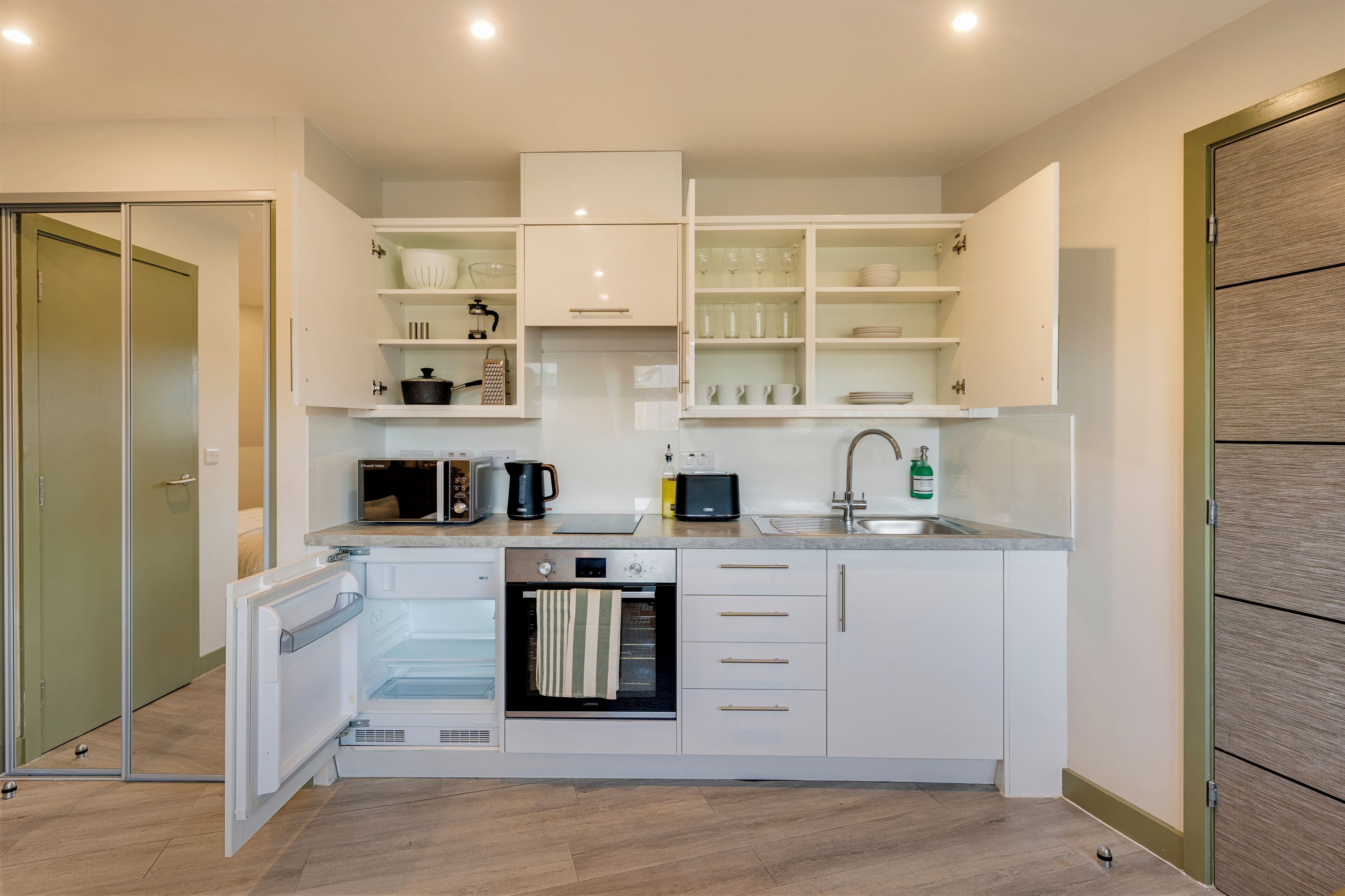 A modern kitchen with white cabinetry, a built-in oven, a microwave, and a sink.