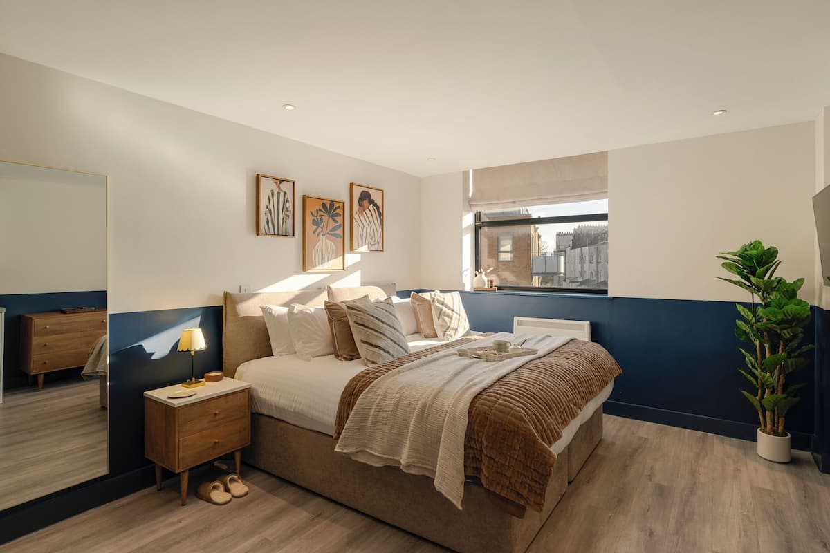 Ein Schlafzimmer mit Bett, Nachttisch, Lampe und einer Topfpflanze.