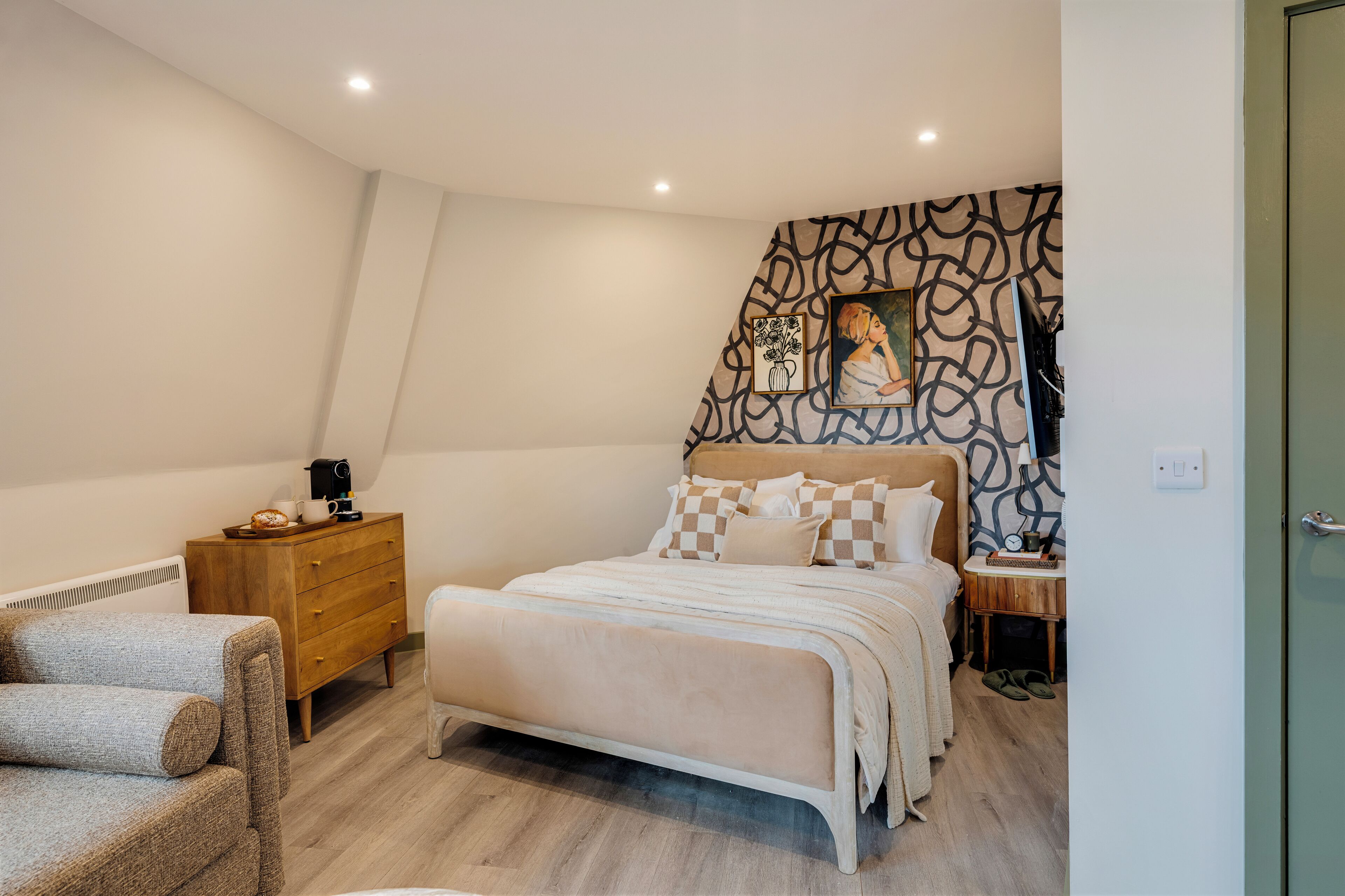 Una camera da letto con un letto, una cassettiera, una sedia, un comodino e una parete con motivo geometrico.