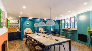Un restaurant moderne avec une longue table en bois, des murs bleus et des luminaires suspendus.