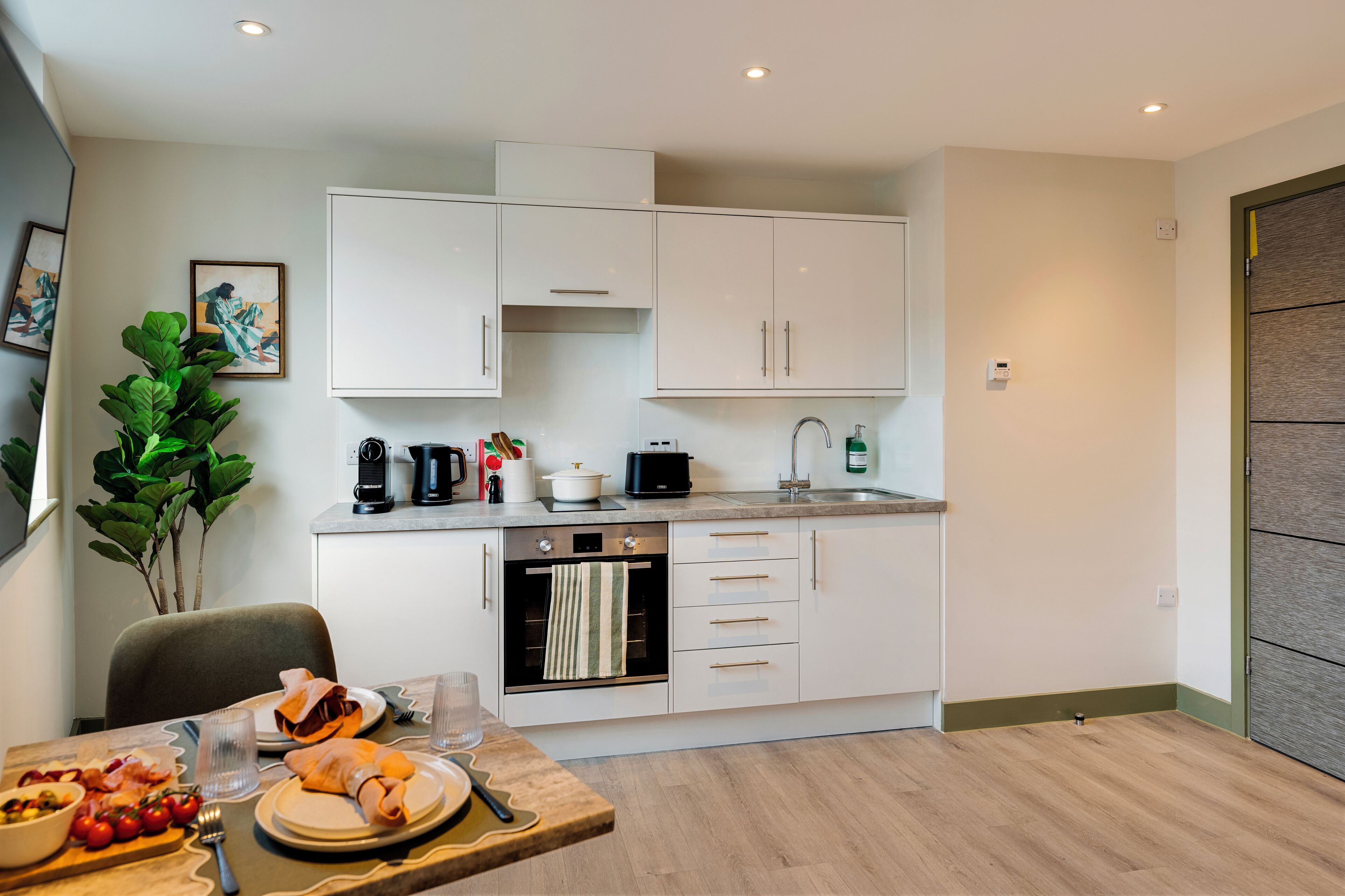 A modern kitchen with white cabinets, a built-in oven, and a dining area with a table set for a meal.