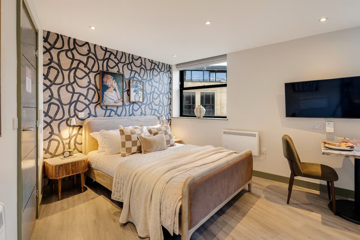 Ein modernes Schlafzimmer mit Bett, Nachttischen, einem Sessel, einem Fernseher und einem Fenster.