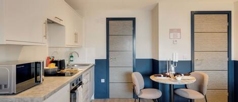 Una cocina compacta con microondas, lavamanos y armarios. Cuenta con un pequeño comedor con dos sillas y una mesa.