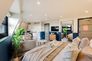 Une chambre d’hôtel moderne dotée d’un grand lit, d’un petit coin salon, d’une kitchenette et d’une salle de bain.