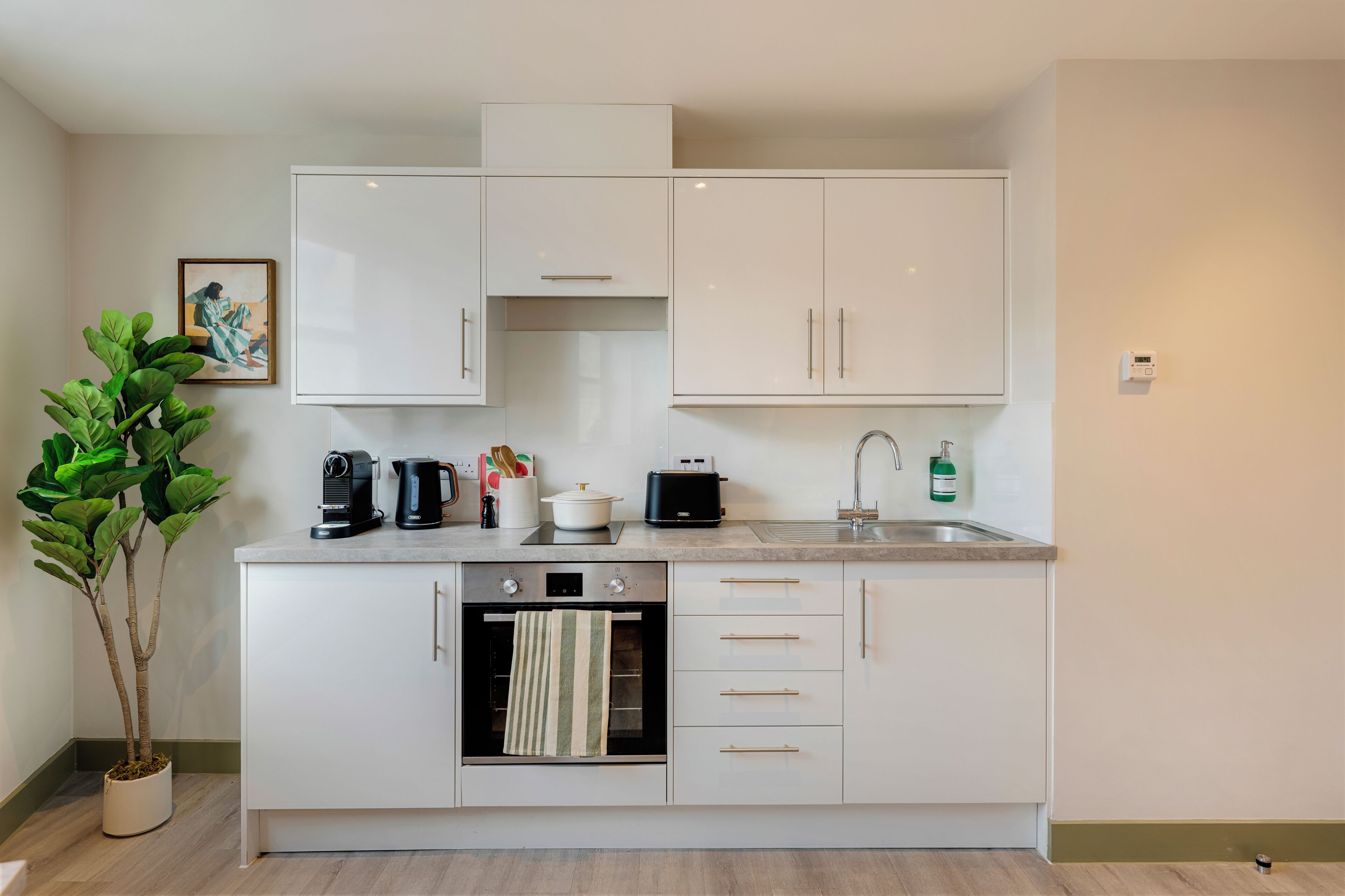 A modern kitchen with white cabinets, a built-in oven, a coffee maker, a toaster, and a sink.