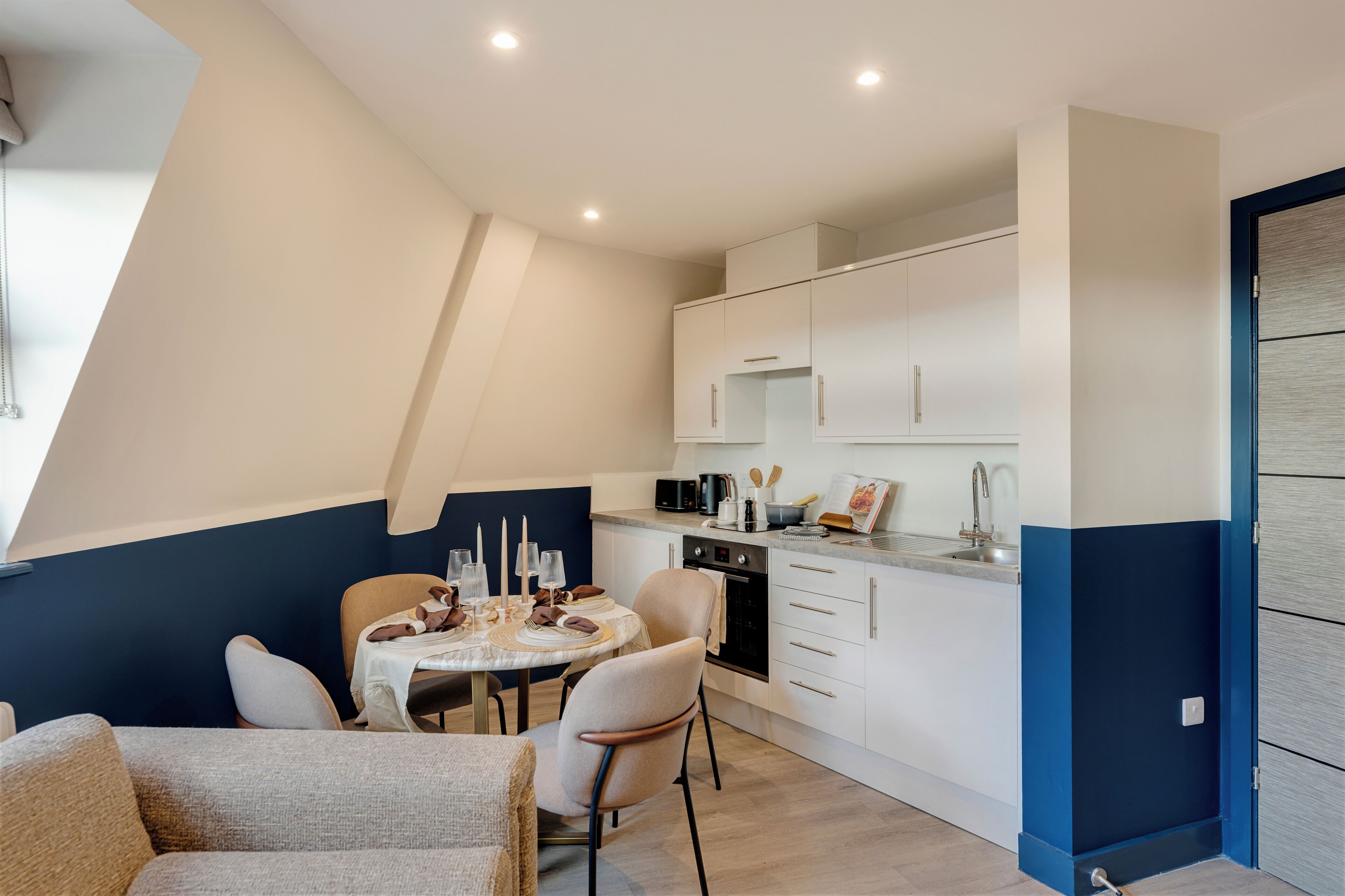 Una cocina moderna con armarios blancos, una mesa de comedor para cuatro personas y una pared de acento azul.