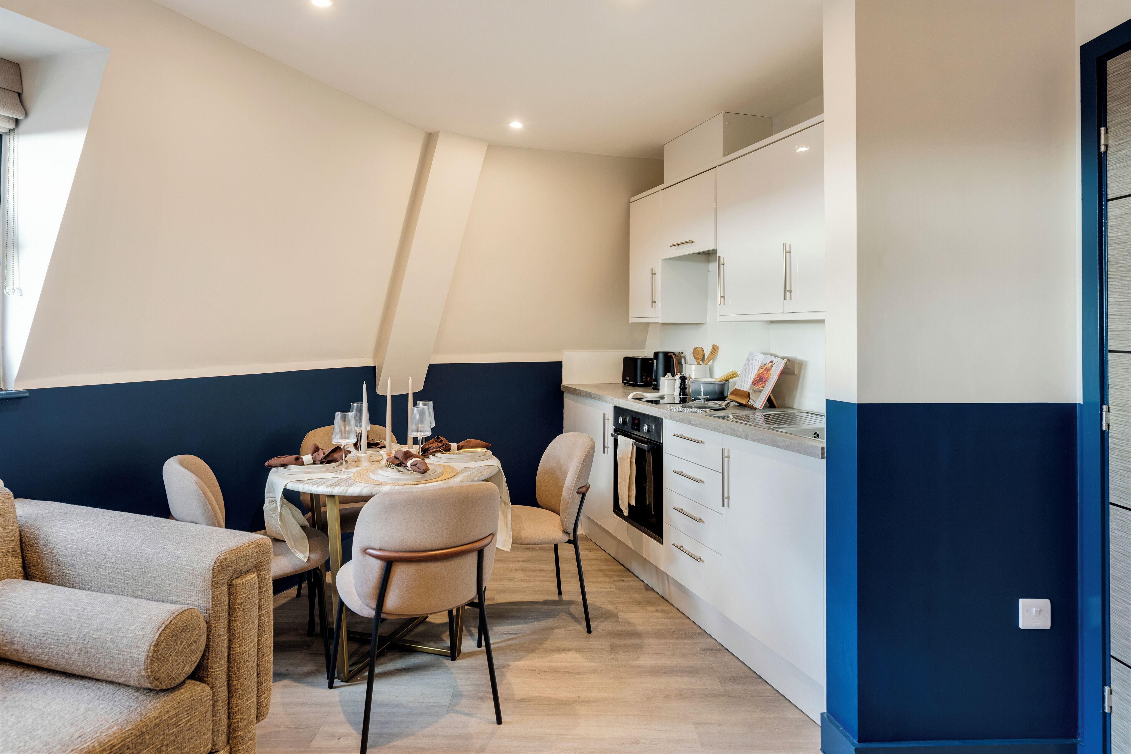 A modern kitchen with white cabinets, a dining area with a table set for two, and a blue accent wall.
