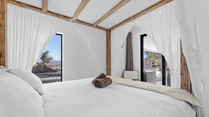 A bedroom with a large bed, sheer curtains, and a view of a rocky landscape. - Villa Odo - Luxury villa with heated pool (Lajares)