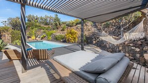 A poolside area with a hammock, lounge chairs, and a view of a pool and garden. - Villa Odo - Luxury villa with heated pool (Lajares)