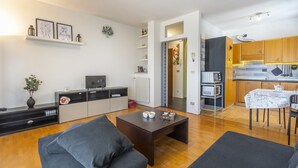 Ett modernt vardagsrum med en soffa, ett soffbord och en tv. Det finns också ett köksområde med träskåp och ett matbord.