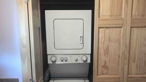 A compact laundry room with a washing machine and dryer, wooden cabinets, and a small chair.