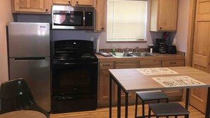 A compact kitchen with wooden cabinets, a stainless steel refrigerator, a microwave, a stove, a sink, and a dining area with a table and chairs.
