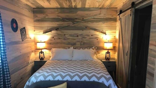Una habitación acogedora con una cama, dos mesitas de noche con lámparas y paredes de madera.