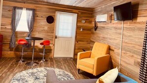Una habitación acogedora con paredes de madera, una puerta, un televisor, una silla roja, una mesita y una alfombra estampada.