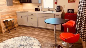 Une cuisine compacte équipée d’un four à micro-ondes, d’un évier et d’un petit coin repas avec une table et deux chaises rouges.