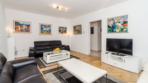 Una sala de estar moderna con un sofá de cuero negro, una mesa de centro blanca, un televisor de pantalla plana sobre un mueble blanco y varias pinturas en las paredes.