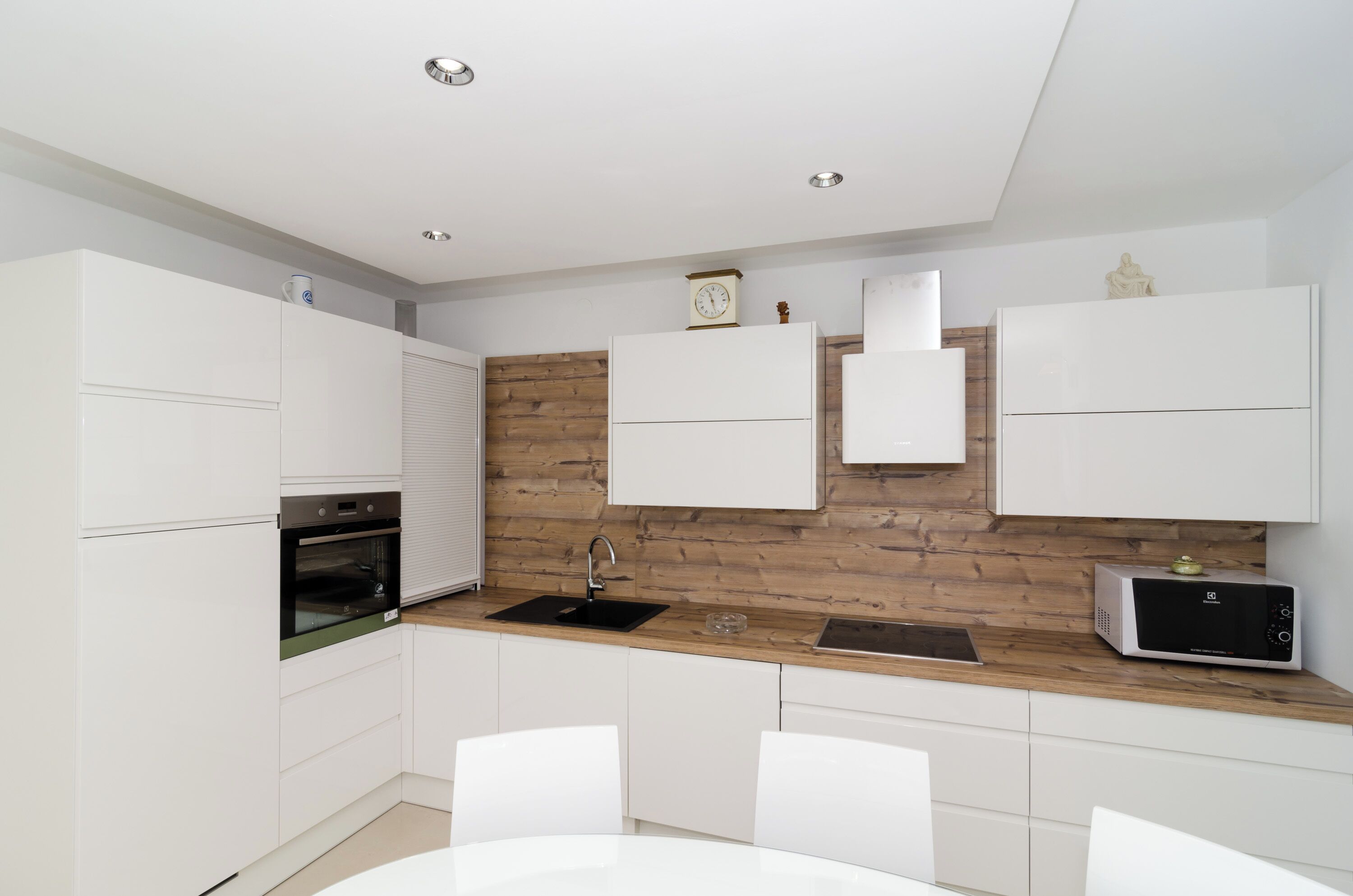 A modern kitchen with white cabinetry, a wooden accent wall, a built-in oven, a microwave, and a sink.