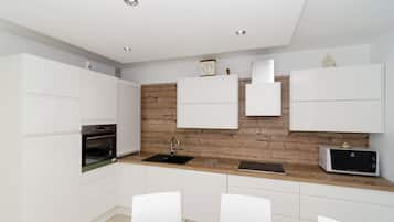 A modern kitchen with white cabinetry, a wooden accent wall, a built-in oven, a microwave, and a sink.