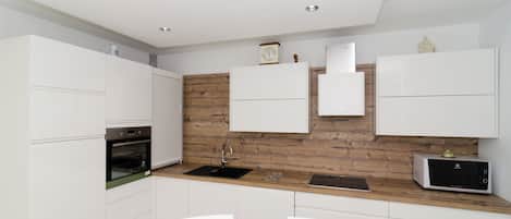 A modern kitchen with white cabinetry, a wooden accent wall, a built-in oven, a microwave, and a sink.