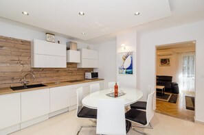 A modern kitchen with white cabinets, a wooden countertop, and a dining area with a glass table and chairs. - Apartment Iva (Dubrovnik)