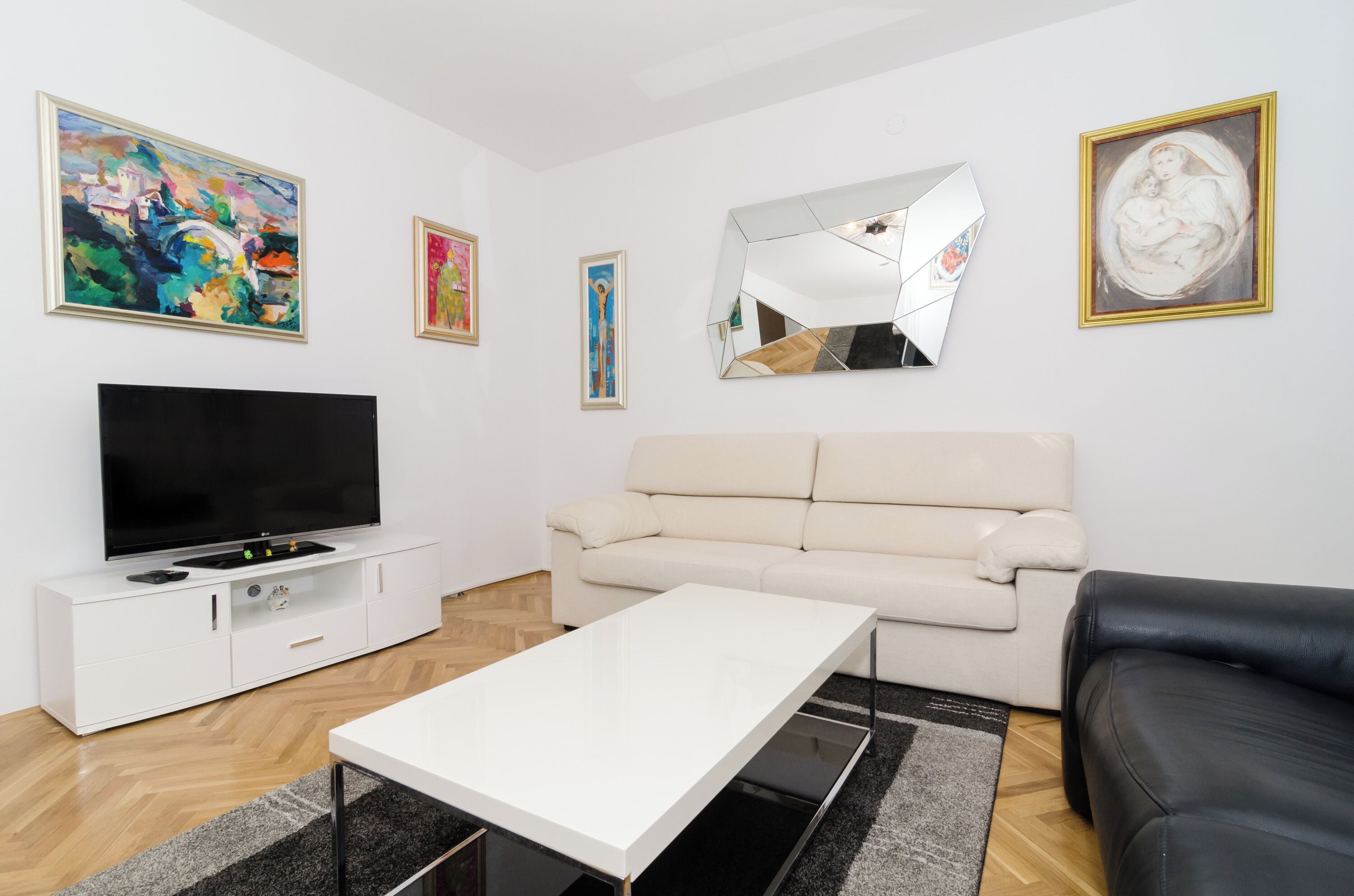 A modern living room with a flat-screen TV, a beige sofa, a white coffee table, and artwork on the walls.