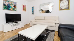 Una sala de estar moderna con una televisión de pantalla plana, un sofá color beige, una mesa de centro blanca y obras de arte en las paredes.