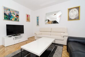A modern living room with a flat-screen TV, a beige sofa, a white coffee table, and artwork on the walls. - Apartment Iva (Dubrovnik)