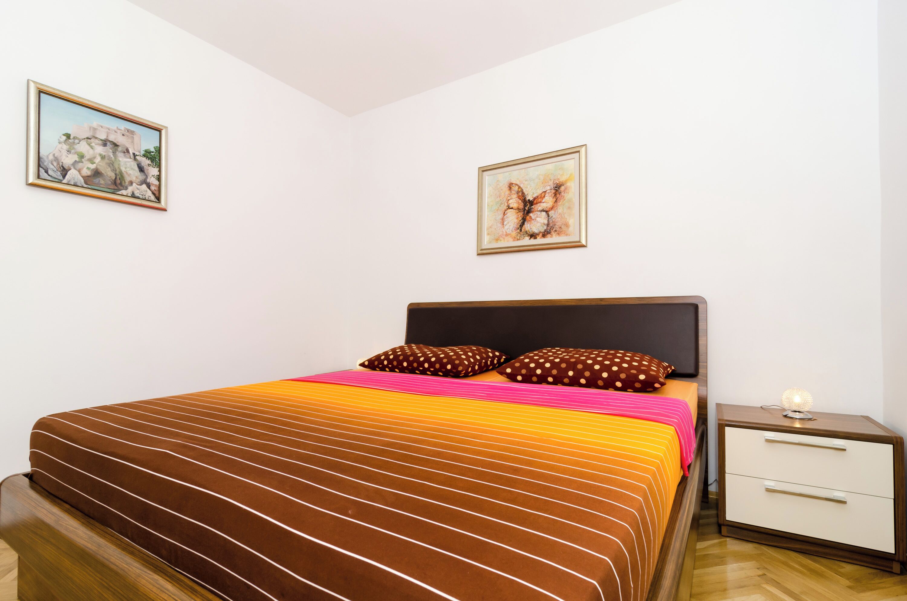 A bedroom with a bed, pillows, a nightstand, and two framed pictures on the wall.