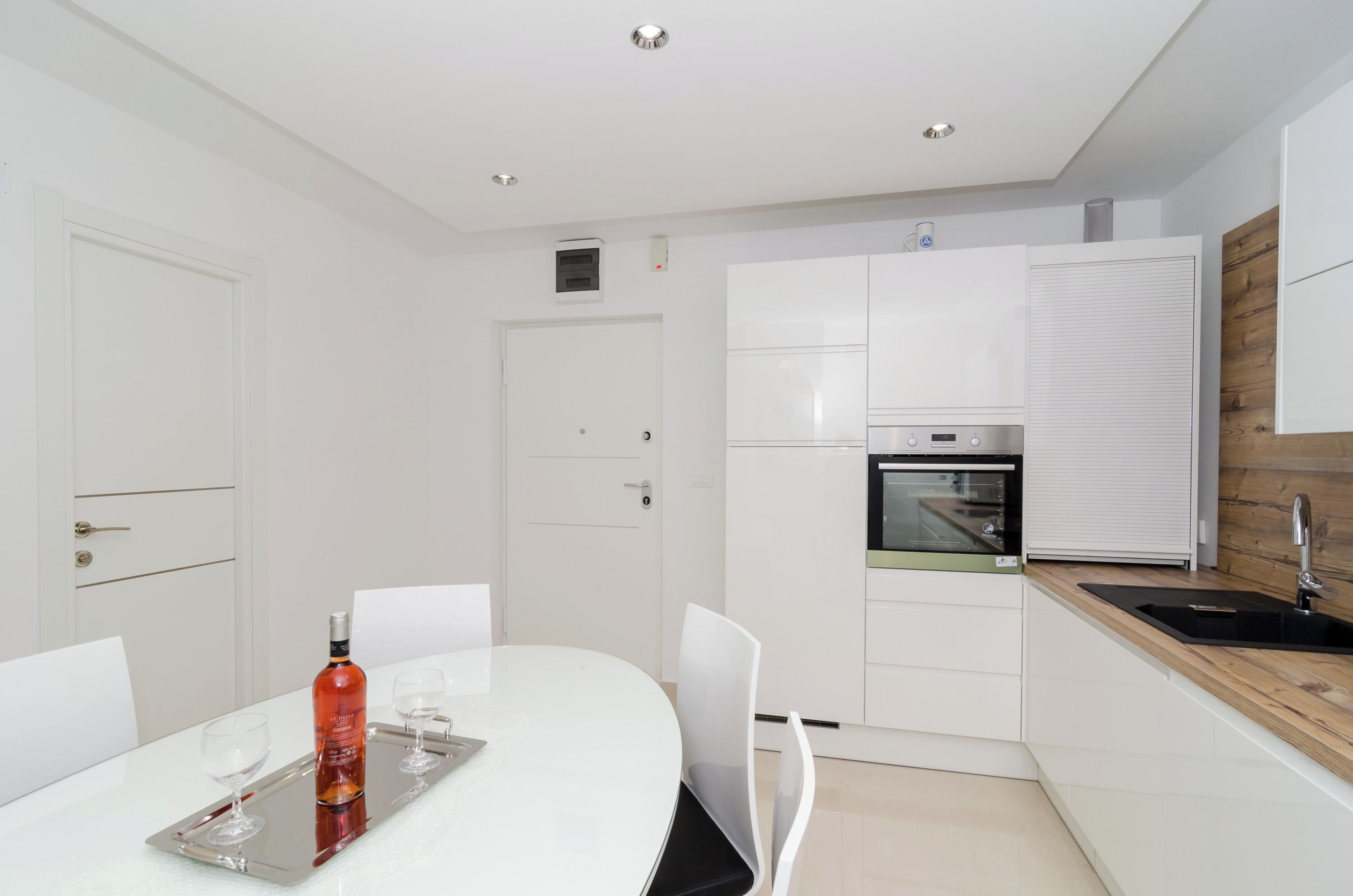 Une cuisine moderne avec des meubles blancs, un four encastré et un mur d’accent en bois.