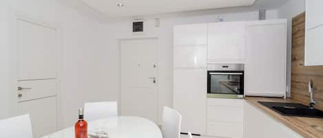 Une cuisine moderne avec des meubles blancs, un four encastré et un mur d’accent en bois.