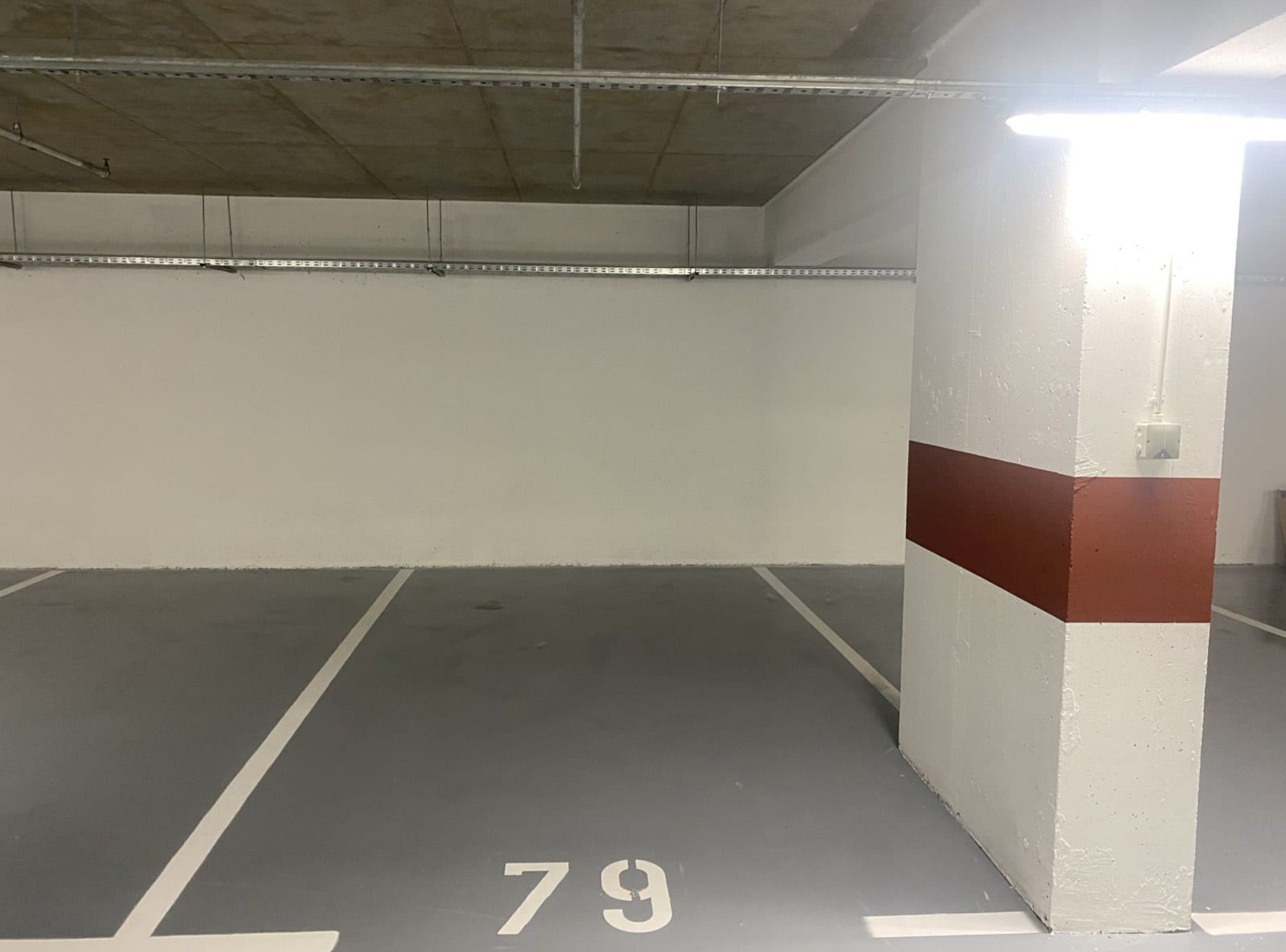 Un estacionamiento vacío con paredes de hormigón, una franja blanca y roja en una pared, y el número 79 pintado en el suelo.