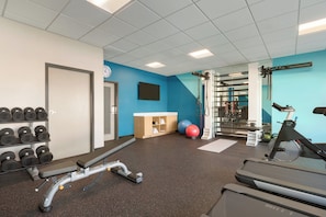 Un gimnasio con equipo de ejercicio, un reloj de pared y una pared azul.