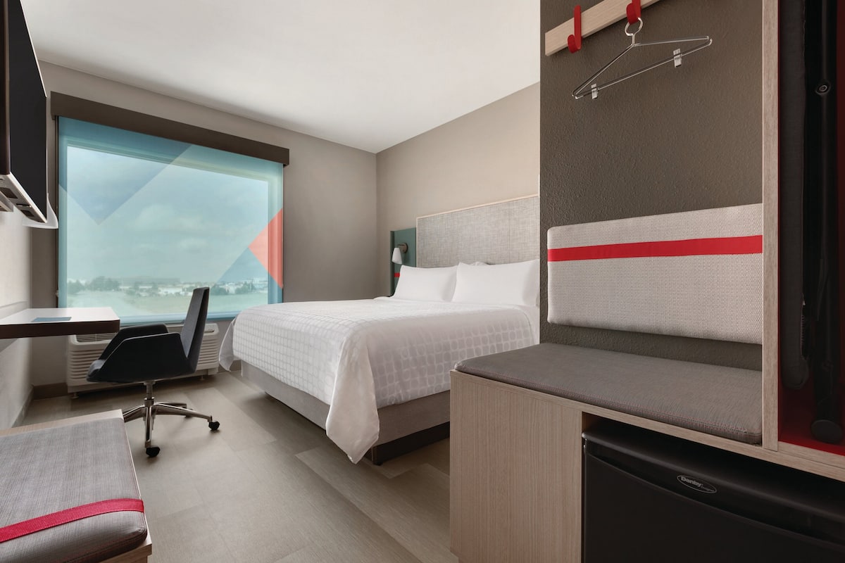 A hotel room with a bed, desk, chair, and a view of the city.