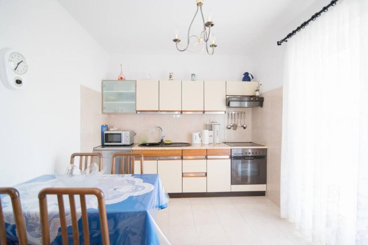 A compact kitchen with a microwave, toaster, kettle, and oven. There is a dining table with chairs and a clock on the wall.