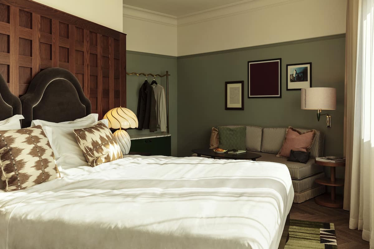 A hotel room with a large bed, a sofa, a small table, and a lamp.