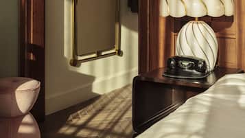 A hotel room with a wooden door, a mirror, a bedside table with a lamp, and a telephone.
