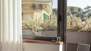 A hotel room with a balcony, a dining table with a chair, and a view of a building and trees.