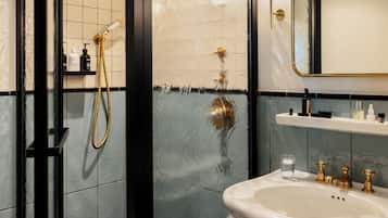 Un baño con cabina de ducha de vidrio, un lavabo blanco con detalles dorados y un espejo con marco dorado.
