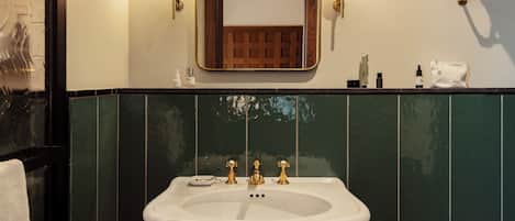 Un baño con un lavabo blanco, baldosas verdes y dos luces fijadas a la pared.