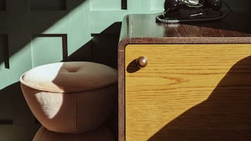A wooden chest of drawers with a telephone on top, a cushioned stool, and a wall with geometric patterns.