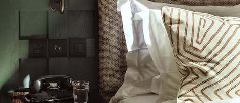 Un lit bien fait, avec une literie à motifs, une lampe de chevet, un téléphone et un verre d’eau posés sur une table de chevet en bois.