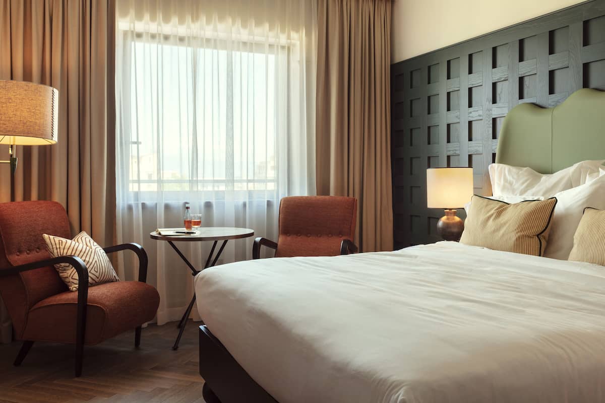 A hotel room with a large bed, two armchairs, a small round table, and a lamp.